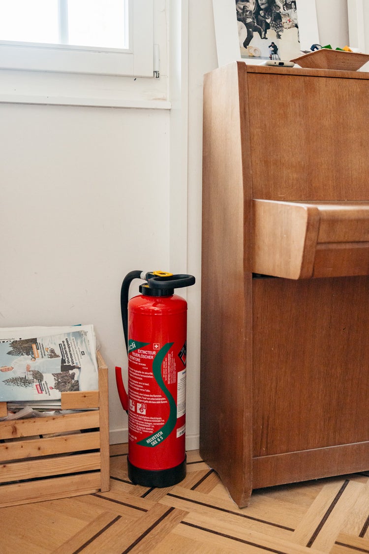 Neben einem Klavier steht ein Handfeuerlöscher.