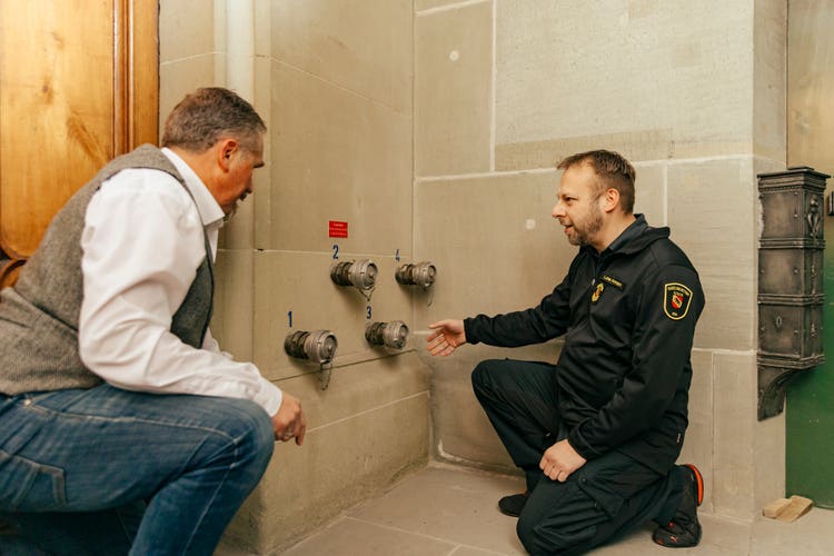 Lukas Ammann zeigt Tino Perotti die vier Anschlüsse, über die Wasser vom Löschfahrzeug in die verschiedenen Bereiche gepumpt wird.