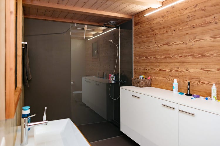 Modernes Badezimmer mit Holzverkleidung und bodenebener Dusche mit Glaswand.