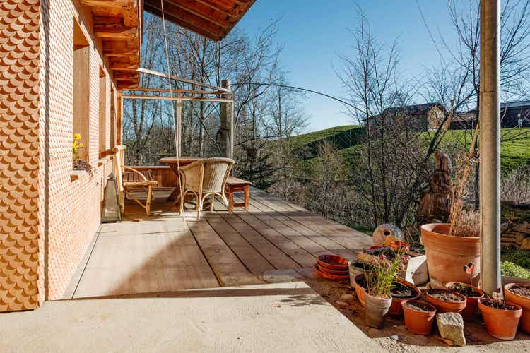 Das Foto zeigt die Ostseite des Hauses. Der untere Teil ist mit runden Holzschindeln bedeckt.