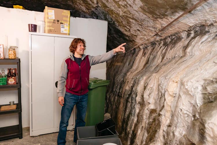 Matthias Müller steht im Keller seines Hauses und zeigt auf die Felswand, an die das Gebäude.