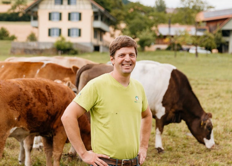 Biobauer Michael Kipfer steht auf der Weide , Kühe grasen im Hintergrund.