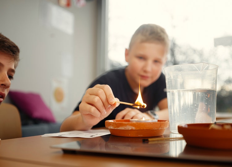 Ein Junge hält ein brennendes Zündholz über eine Kerze.