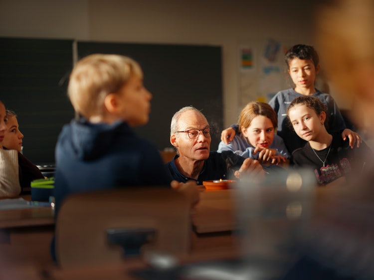 Lehrer Urs Senften führt ein Experiment mit einer Kerze durch, die Schüler:innen schauen gespannt zu.