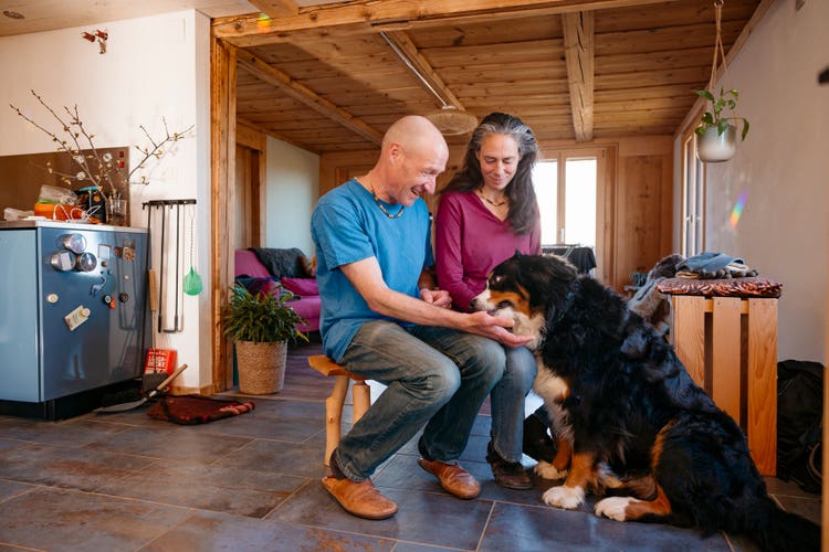 Sandra Haunreiter und Bänz Lüthi sitzen auf einer Bank im Wohnzimmer. Hündin Elly sitzt vor ihnen auf dem Boden.