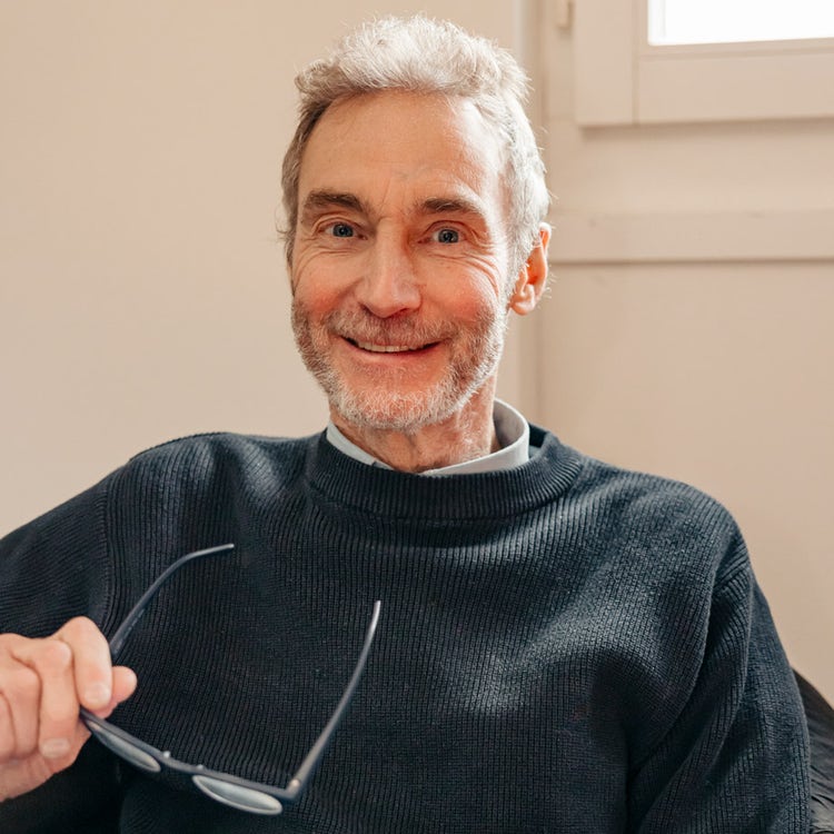 Dag Kappes sitzt mit einem Buch in einem Sessel, die Lesebrille in der Hand.