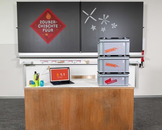 Les trois boîtes de la « Boîte-Feu Magique » sont posées sur le bureau de l’enseignant.