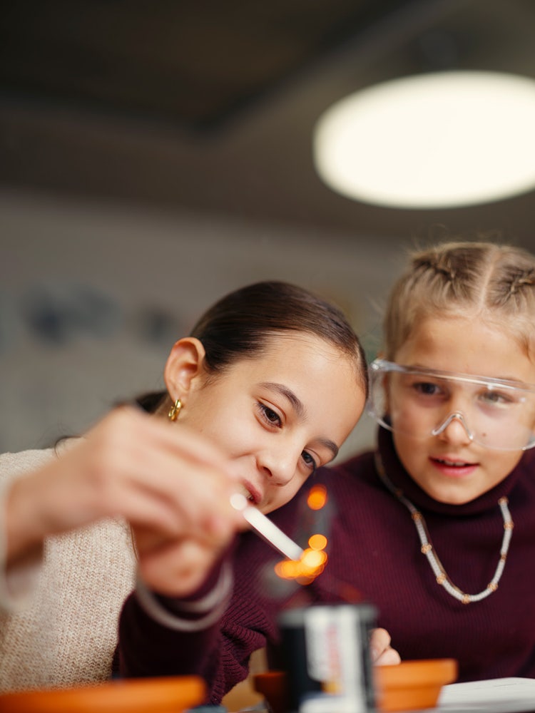 Deux filles tiennent de la laine d’acier contre une batterie et regardent la laine d’acier qui commence à brûler.
