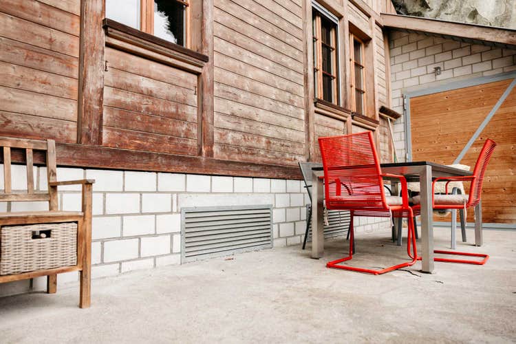 La terrasse de Matthias Müller et les chaises rouges devant le mur en bois de la maison. En bas de la façade, on aperçoit la grille d’aération qui permet à l’air de s’échapper de l’espace situé sous la maison.