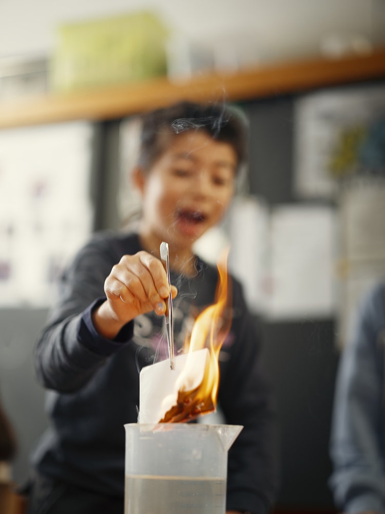 Une élève tient un morceau de papier en feu au-dessus d’un gobelet d’eau à l’aide d’une pincette.