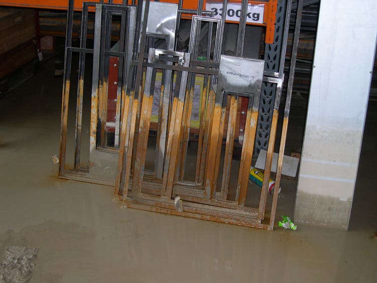Des cadres en acier sont appuyés contre un mur. Ils sont rouillés jusqu’à mi-hauteur.