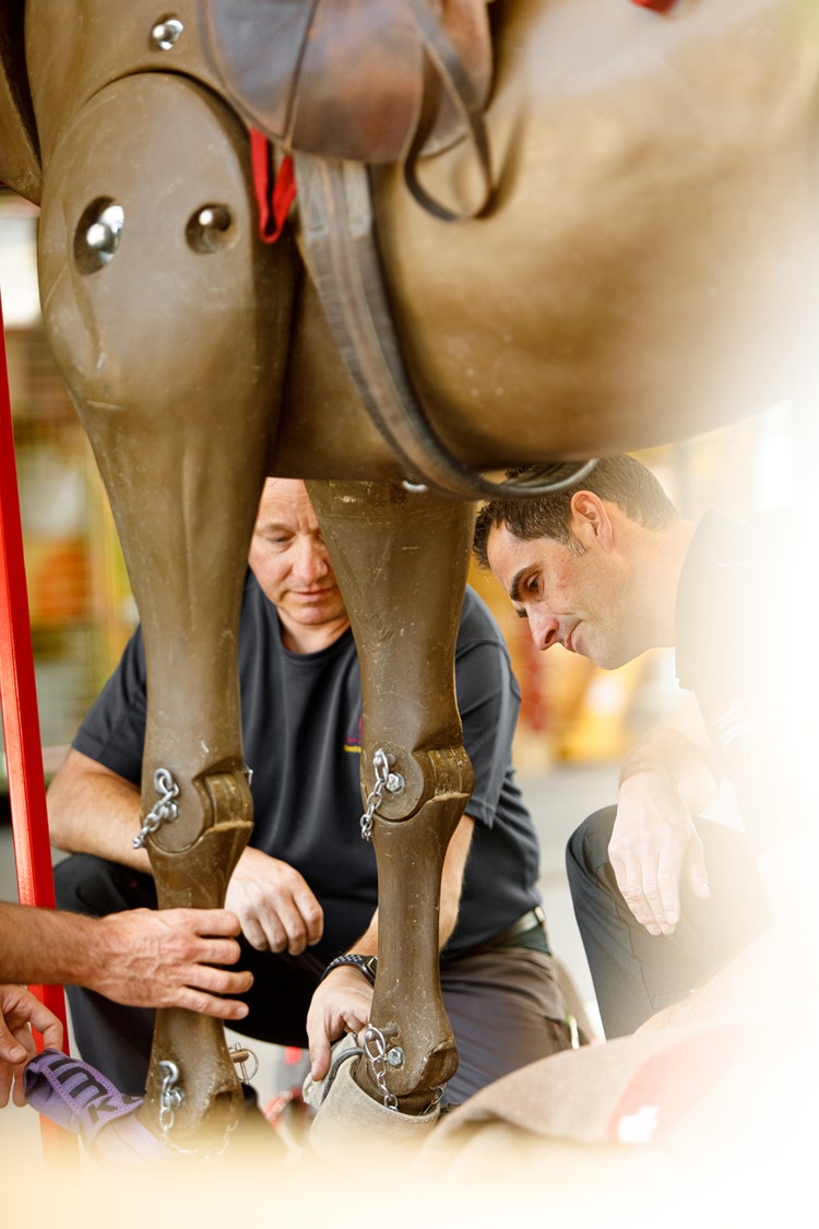 Plusieurs pompiers observent les jambes d’un cheval en plastique grandeur nature.