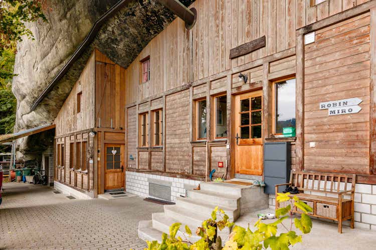 Le Fluehüsli dans la falaise, les marches à l’entrée, le banc devant la façade, et la falaise de grès en saillie.