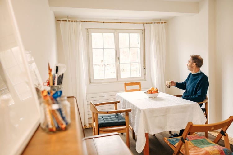 Un homme est assis à la table de la salle à manger avec une tasse et regarde par la fenêtre.