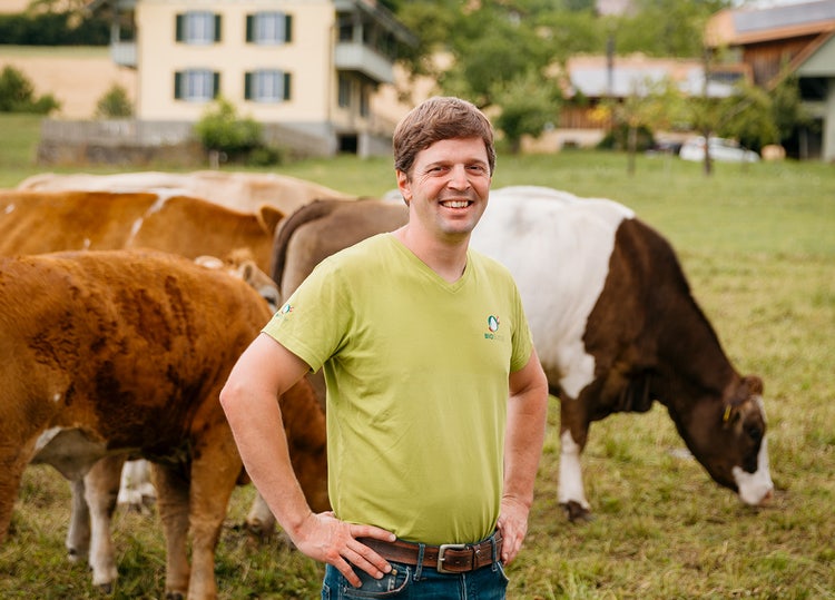 Michael Kipfer, bioagriculteur, dans un pâturage, les vaches paissent en arrière-plan.